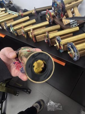 Hand holding a handmade brass kaleidoscope showing the eyepiece end during final assembly in the workshop