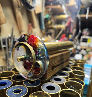 Handmade brass kaleidoscope on the assembly bench beside machined brass tube blanks in the Studio Yabaye workshop